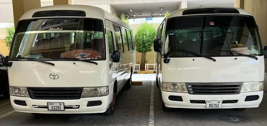 Two Toyota Coaster buses with Dubai number plates parked at the Alsinan Transport depot