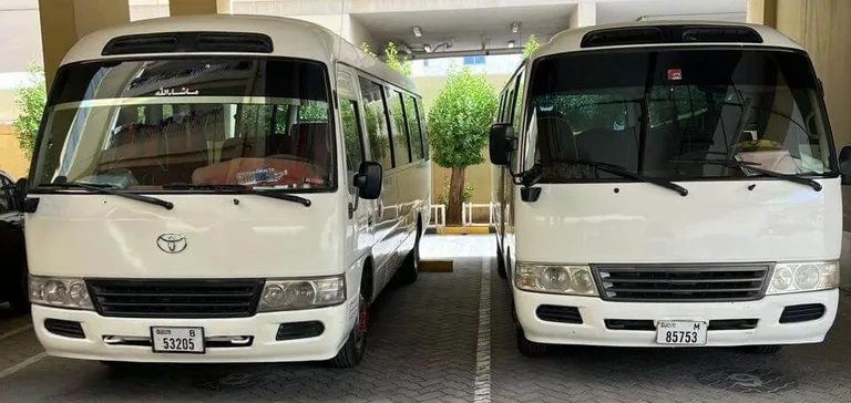 Two Toyota Coaster buses with Dubai number plates parked at the Alsinan Transport depot